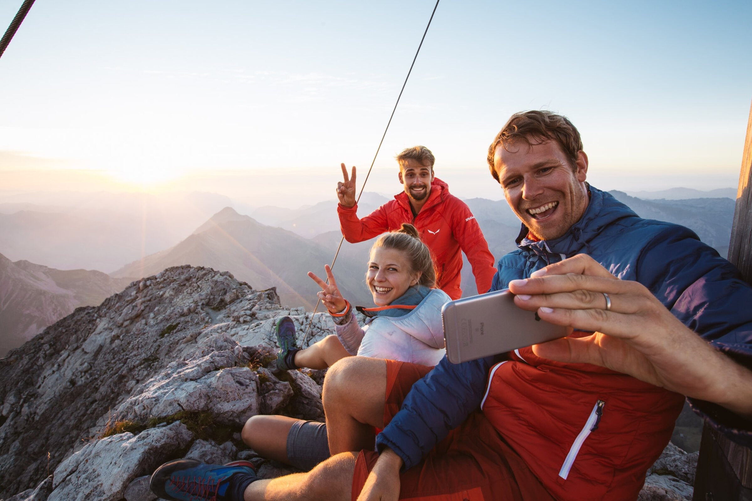 Drei Wandernde am Gipfel bei Sonnenaufgang